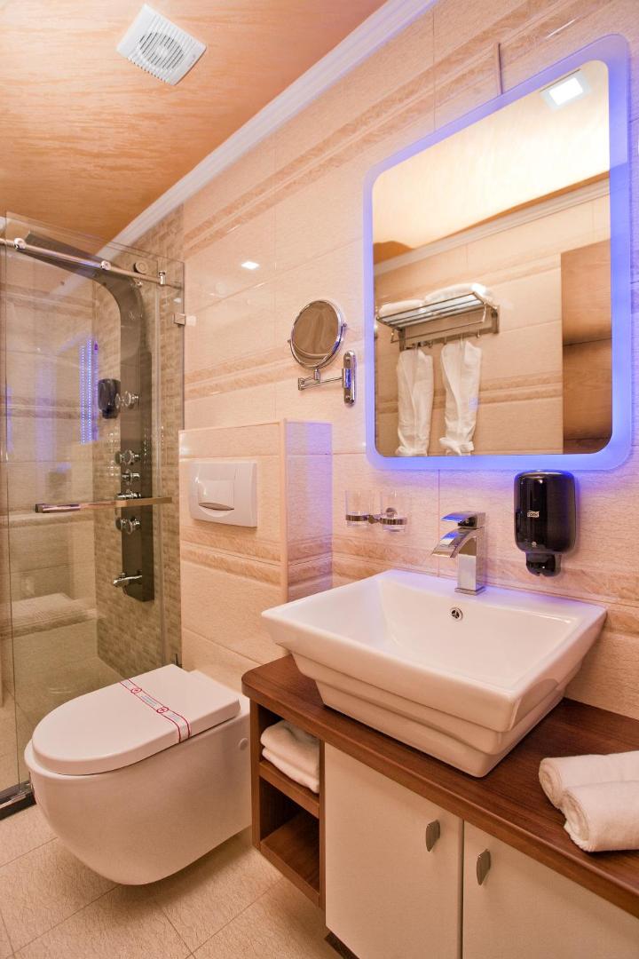 ACD Wellness & Spa numura vannasistaba ar modernu dušas kabīni, izgaismotu spoguli un gaišu flīžu apdari