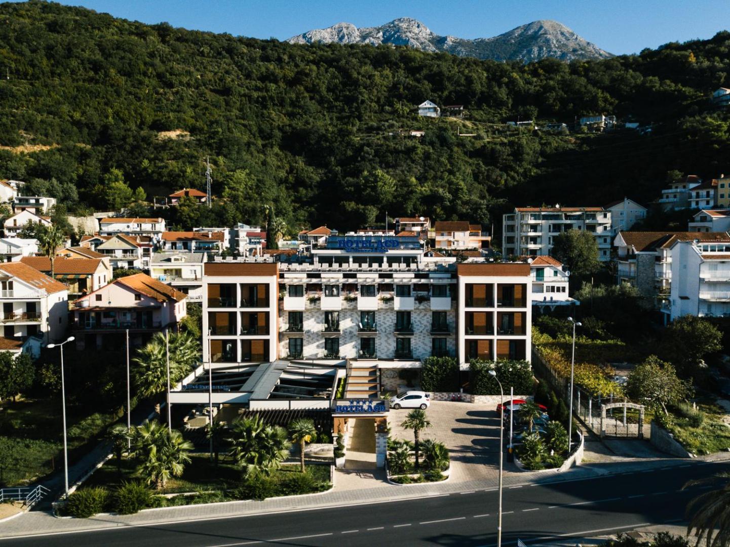 Viesnīcas ACD Wellness & Spa ēka no attāluma uz kalnu un zaļumu fona — redzama arhitektūra un apkārtējā apbūve Melnkalnē