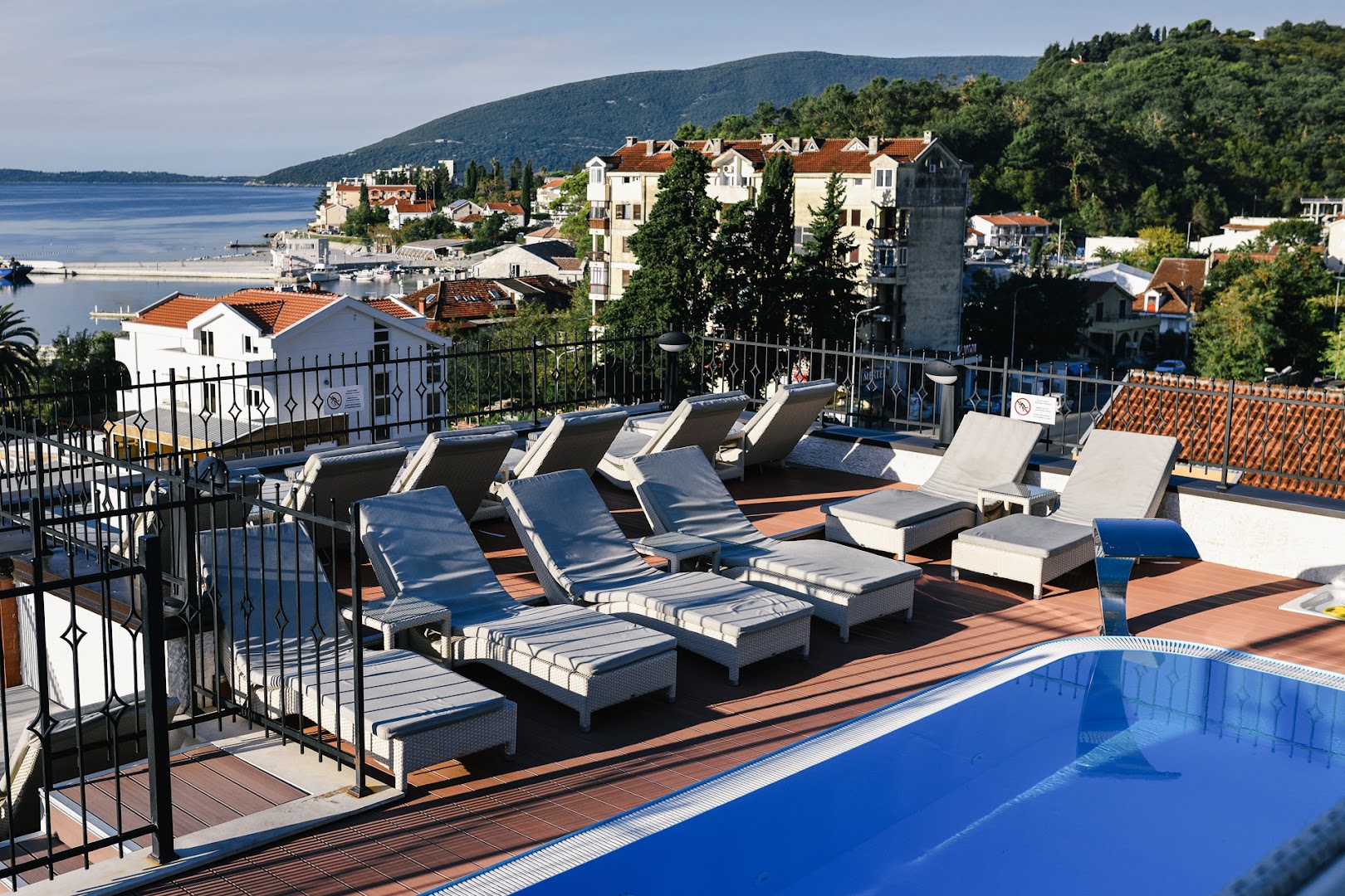Skats no Hotel ACD Wellness & Spa jumta terases uz jūras līci un piekrastes apbūvi — sauļošanās krēsli pie baseina