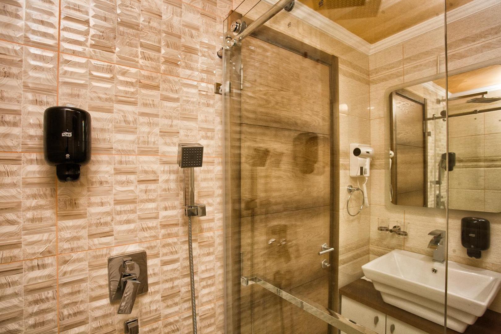 ACD Wellness & Spa viesnīcas numura vannas istaba Melnkalnē ar modernu dušas kabīni, izlietni, spoguli un gaišām flīzēm siltos toņos