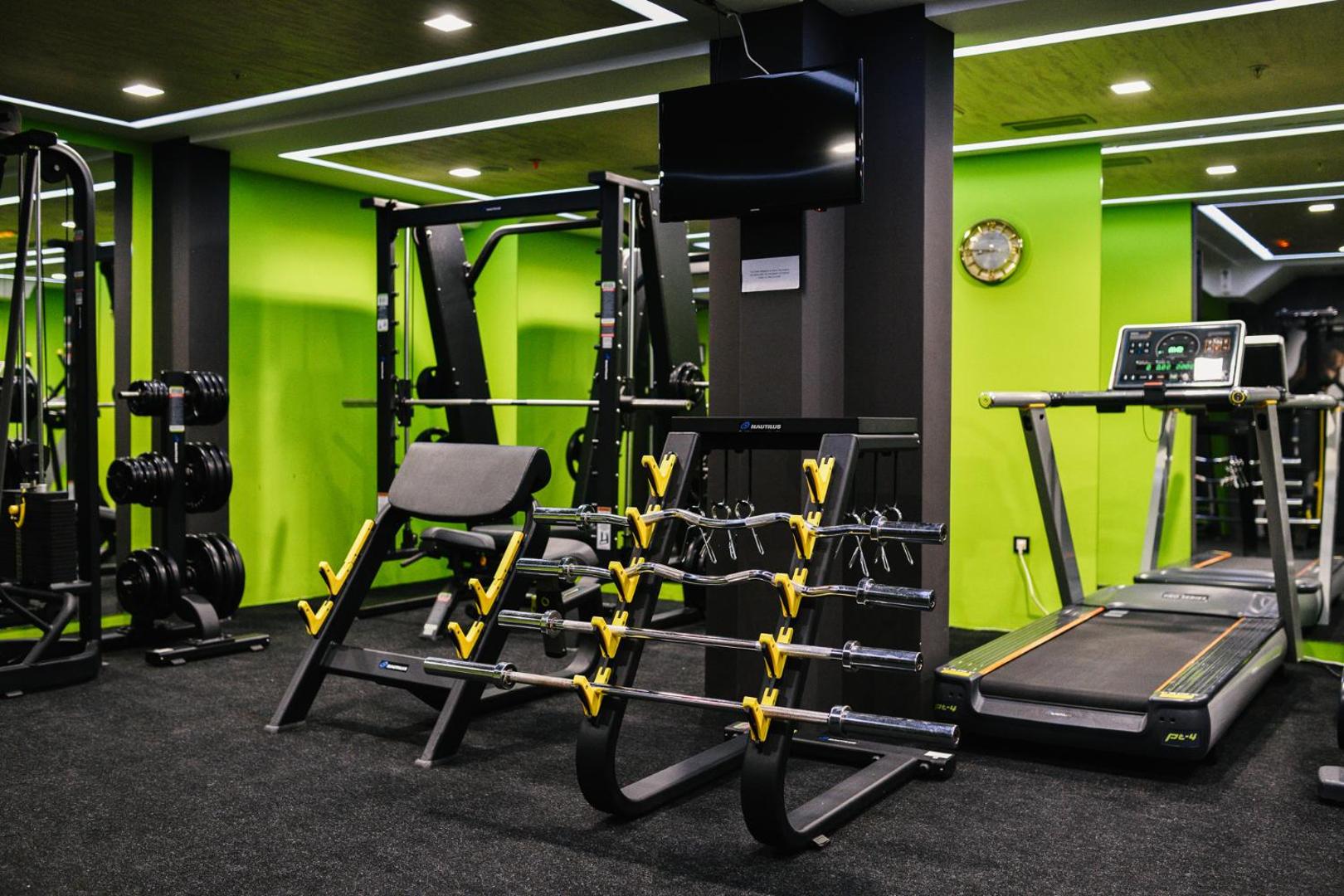 ACD Wellness & Spa modernā fitnesa zāle ar skrejceliņu, svaru stieņiem un spēka trenažieriem košos toņos