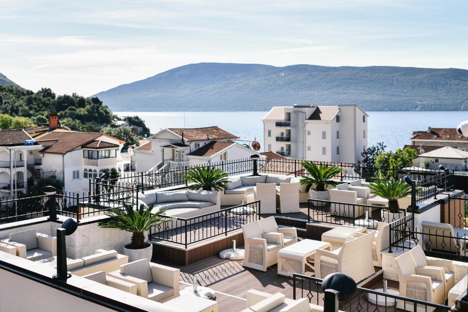 Viesnīcas ACD Wellness & Spa jumta bāra terase ar baltām mēbelēm, palmām podos un skatu uz jūru un kalniem