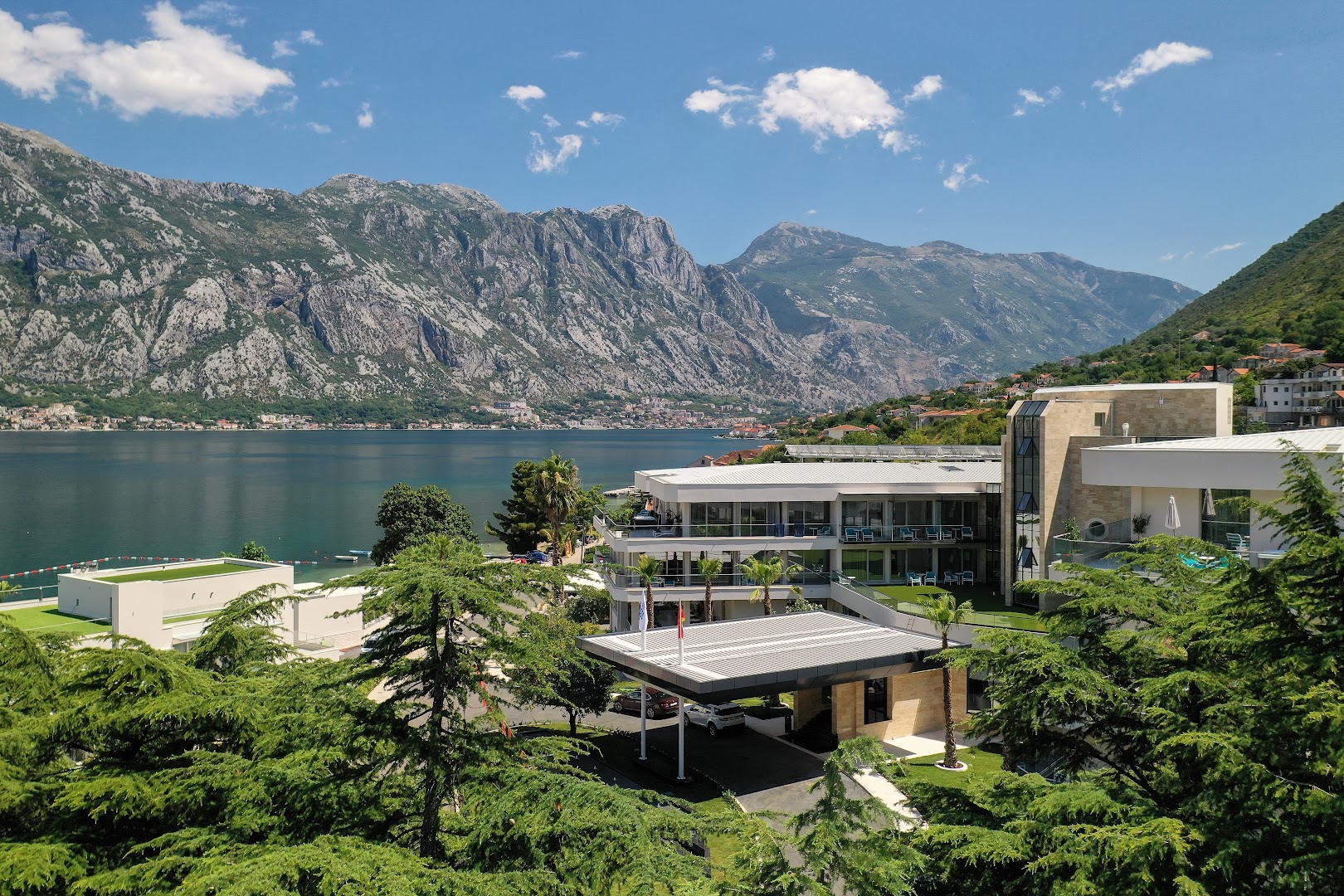 Hyatt Regency Kotor Bay Resort galvenā ieeja un modernā ēka, ko ieskauj zaļi koki un skats uz kalniem