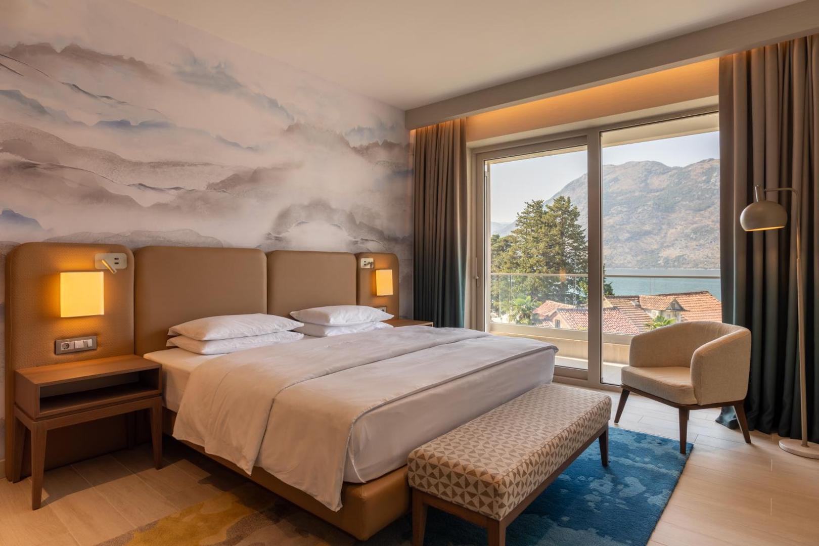Hyatt Regency Kotor Bay Resort moderns numurs ar skatu uz jūru un kalniem — gaišs interjers, liela gulta un balkons