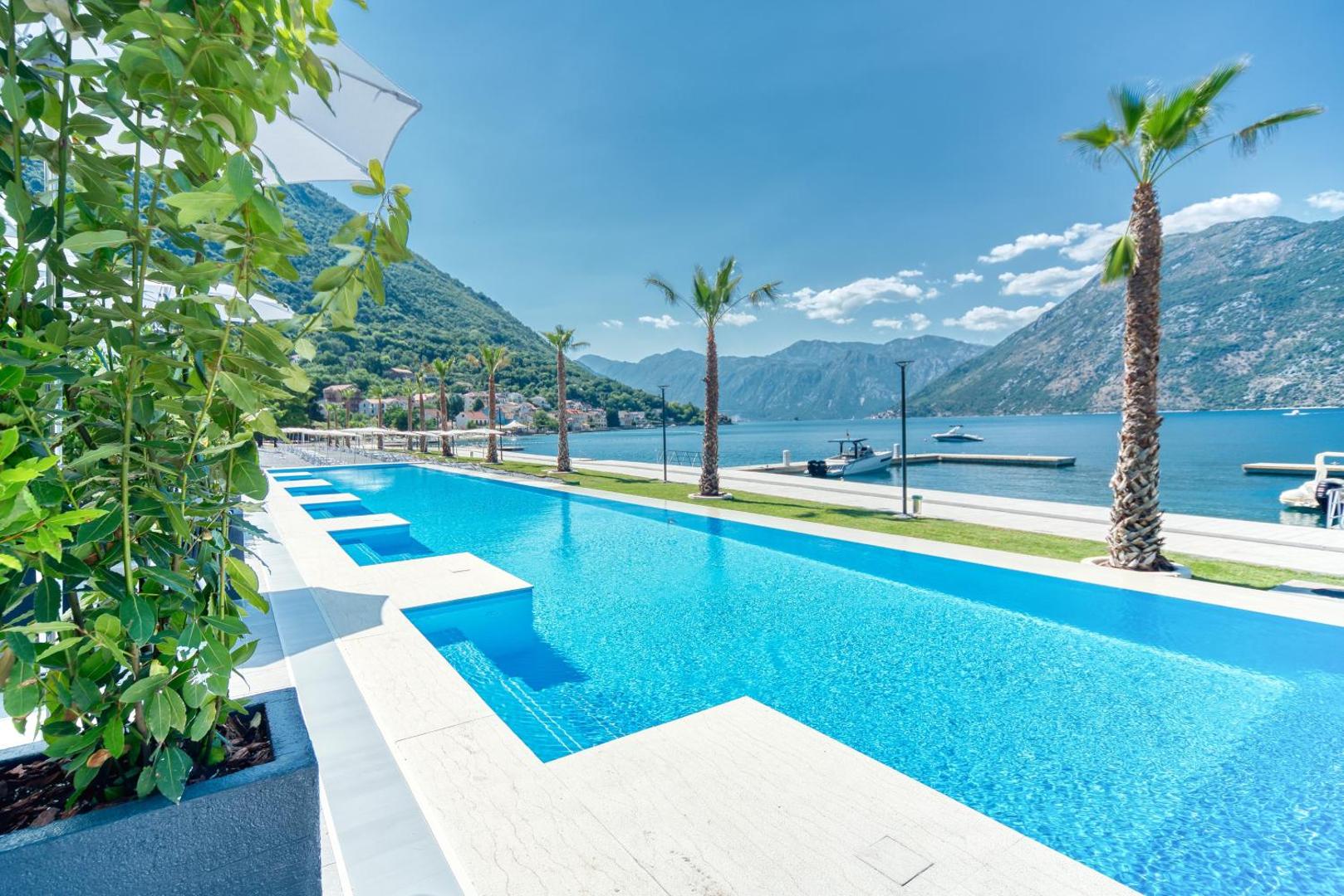 Hyatt Regency Kotor Bay Resort garais āra baseins piekrastē ar palmām un skatu uz kalniem un jahtu piestātni