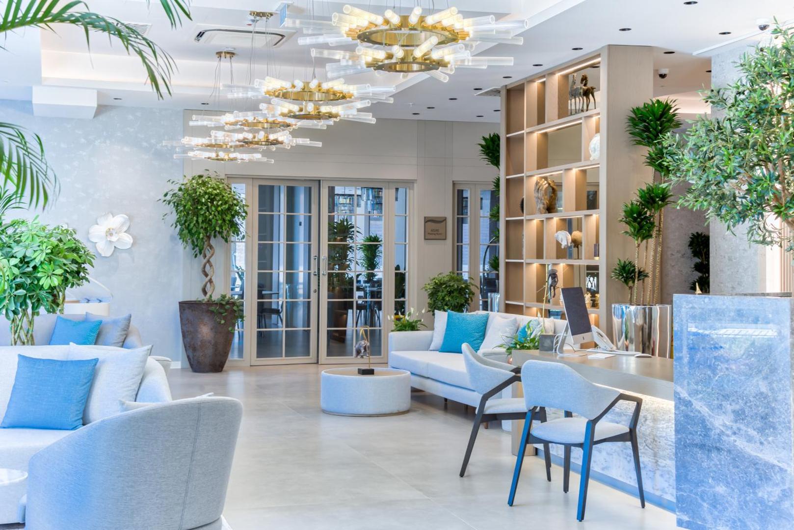 Hyatt Regency Kotor Bay Resort gaišais vestibils ar atpūtas zonu, dīvāniem un dizaina lustrām — moderna viesnīcas recepcijas zona