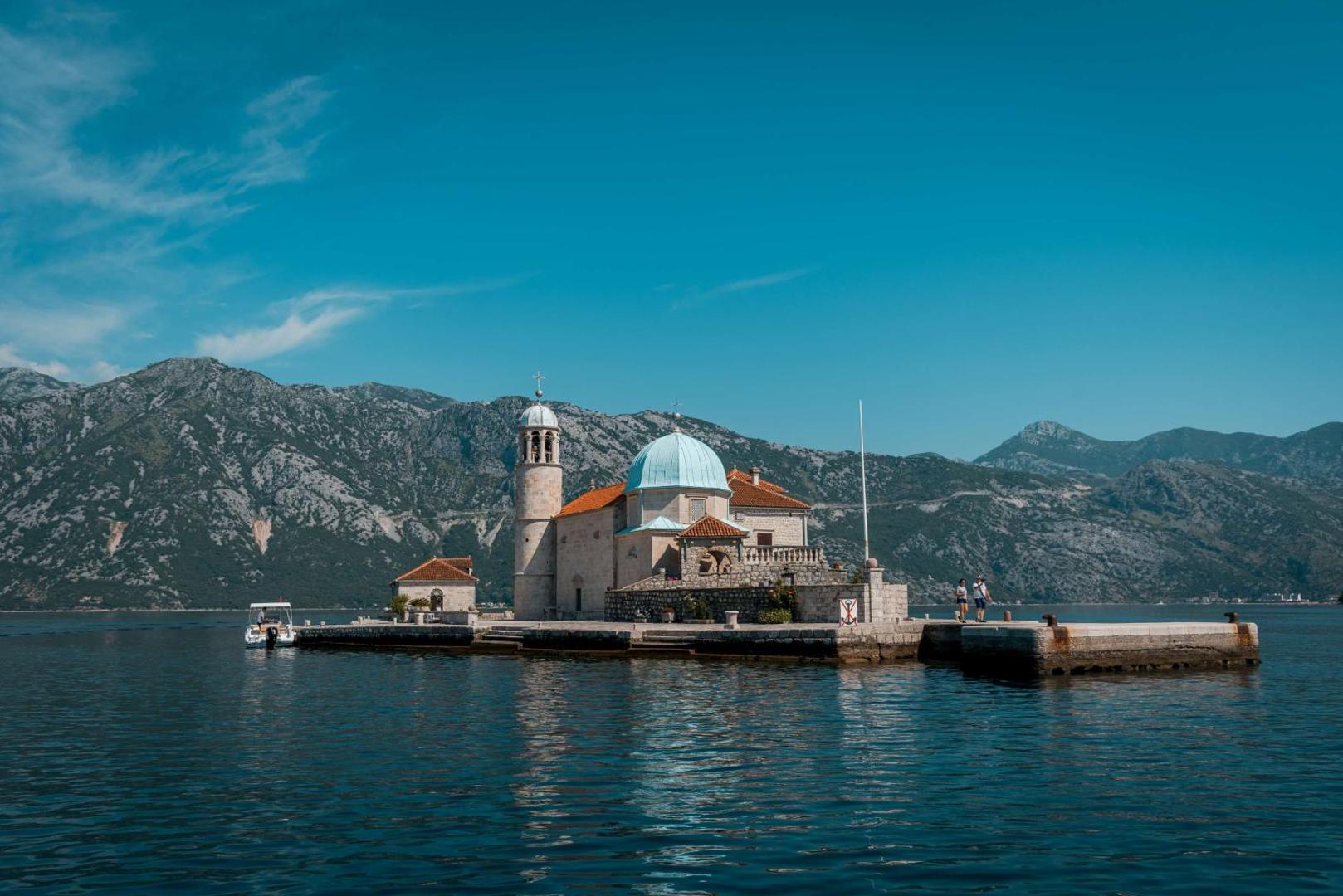 Hyatt Regency Kotor Bay Resort skats uz Gospa od Škrpjela baznīcu Kotoras līcī Melnkalnē — vēsturiska sala uz kalnu fona