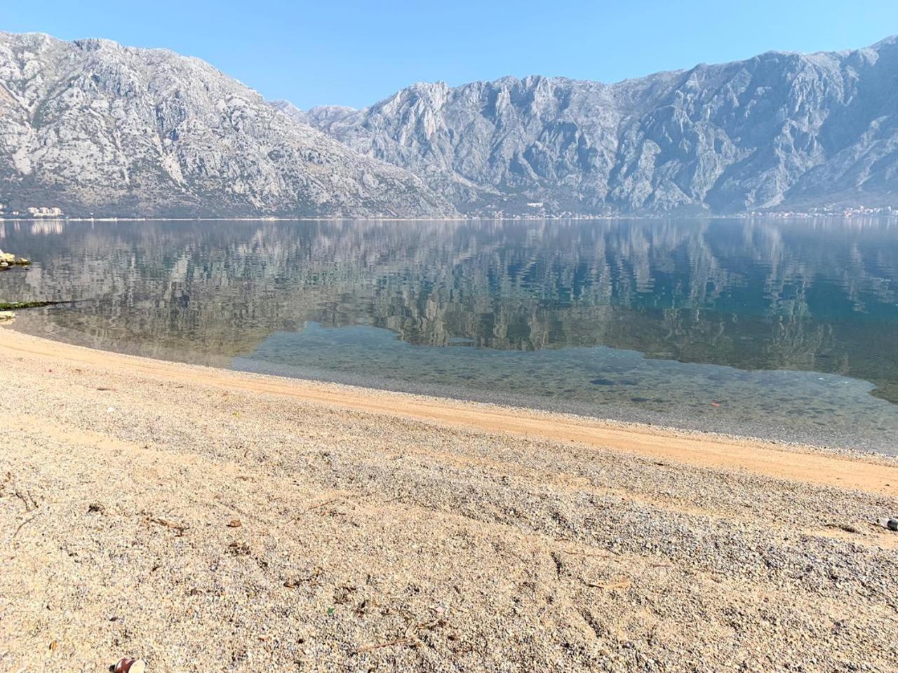 Hyatt Regency Kotor Bay Resort oļu pludmale ar kristāldzidru ūdeni un kalnu grēdu atspulgu mierīgajā līcī