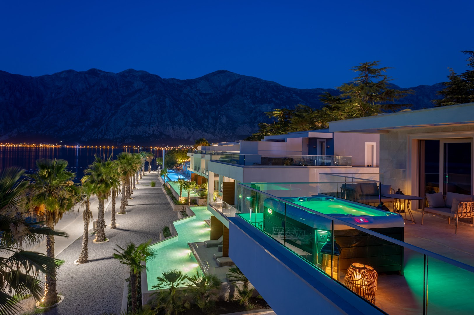 Hyatt Regency Kotor Bay Resort terase ar džakuzi un baseinu apgaismojumu vakarā, skats uz naksnīgo līci un kalniem