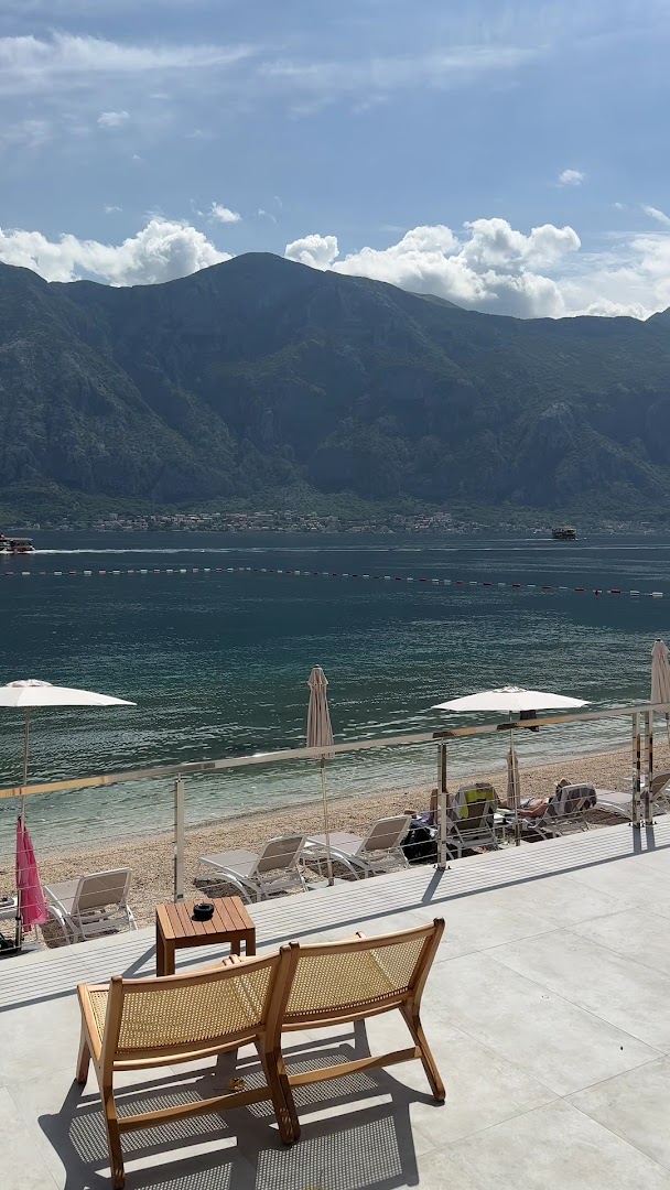 Skats no Hyatt Regency Kotor Bay Resort terases uz oļu pludmali, saulessargiem un majestātiskiem kalniem pāri Kotoras līcim