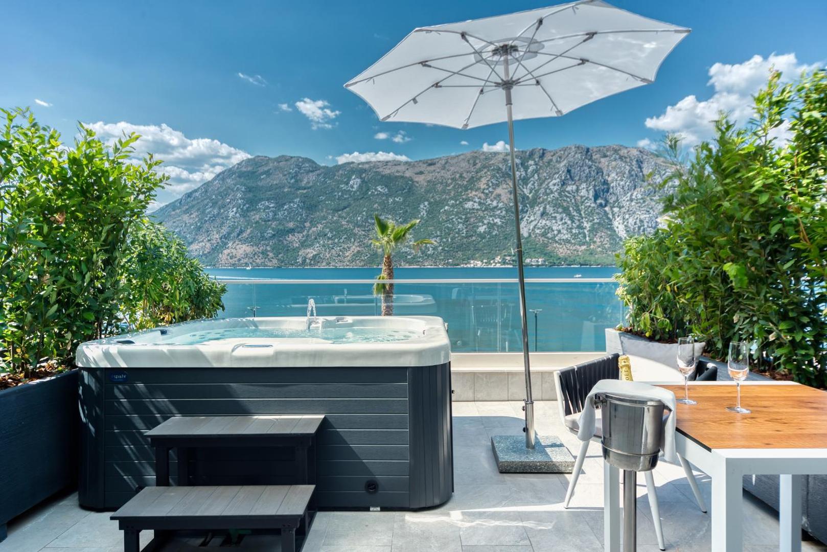 Hyatt Regency Kotor Bay Resort āra terase ar džakuzi, galdiņu un skatu uz kalniem saulainā dienā