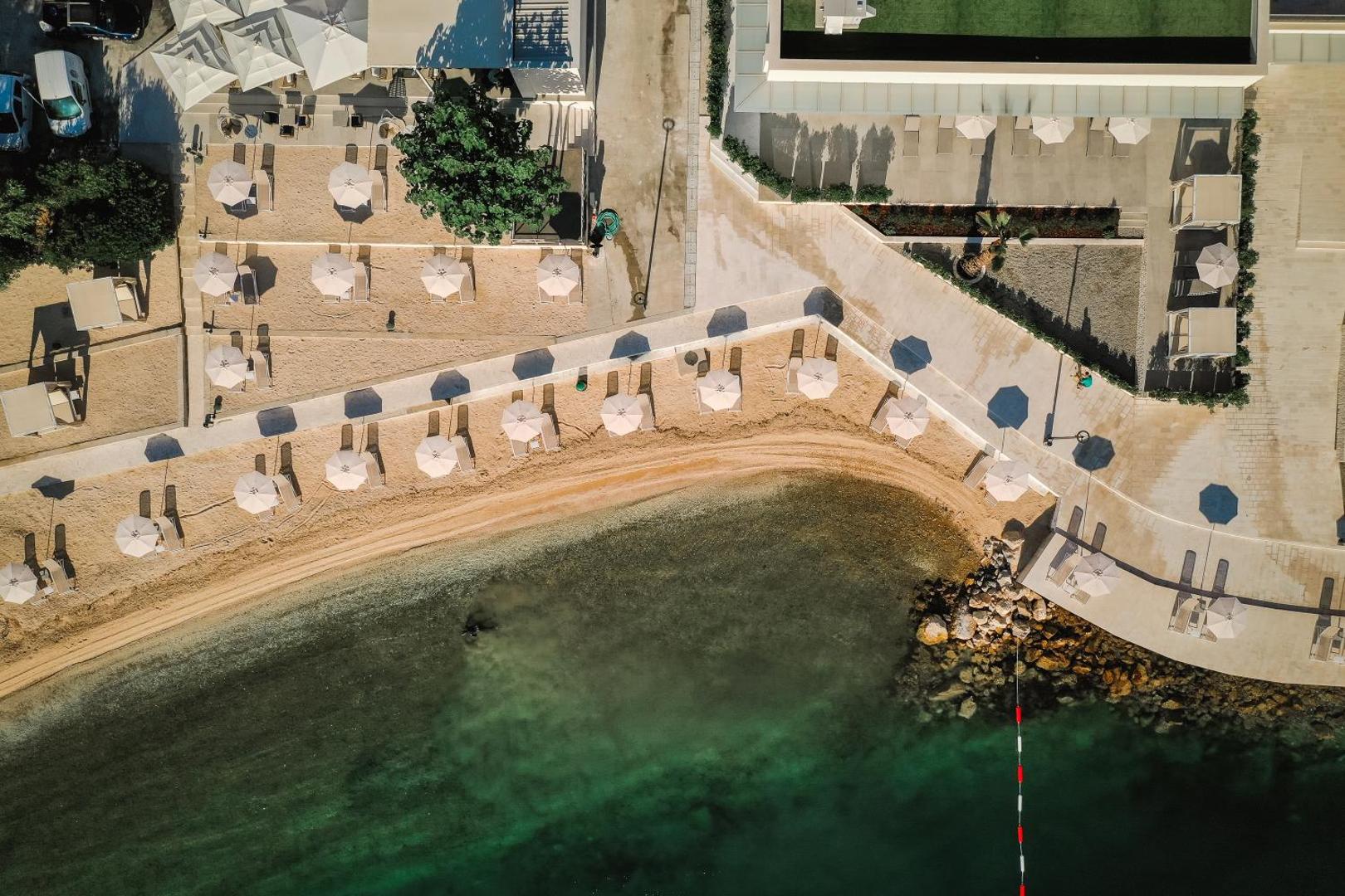 Hyatt Regency Kotor Bay Resort pludmales zonas skats no putna lidojuma — saulessargi, sauļošanās krēsli un tirkīza ūdens