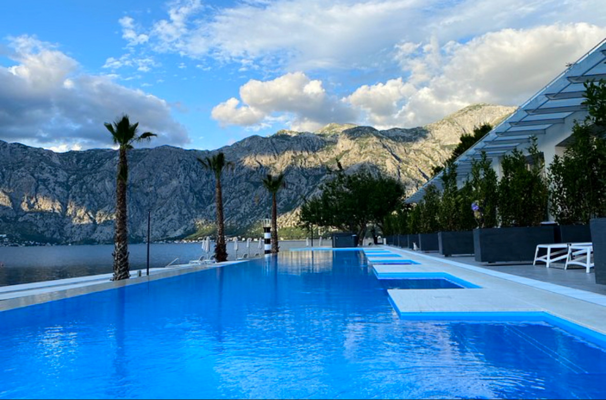 Hyatt Regency Kotor Bay Resort bezmalas baseins krēslas stundā ar skatu uz augstajām Melnkalnes kalnu virsotnēm un līci