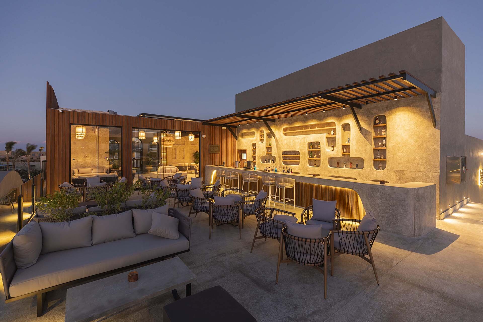 Sunrise Tucana Resort atvērta tipa jumta bārs ar modernu apgaismojumu, mīkstajām mēbelēm un stilīgu leti saulrieta laikā Hurgadā.