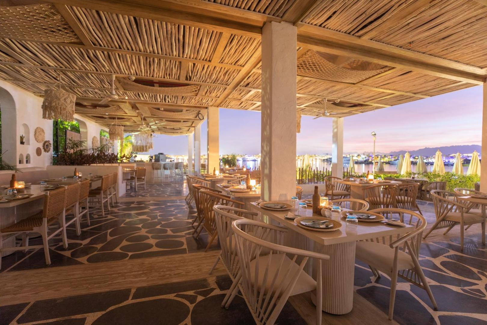 Sunrise Tucana Resort āra terases restorāns vakarā ar skatu uz izgaismoto piekrasti, koka griestu apdari un romantisku apgaismojumu