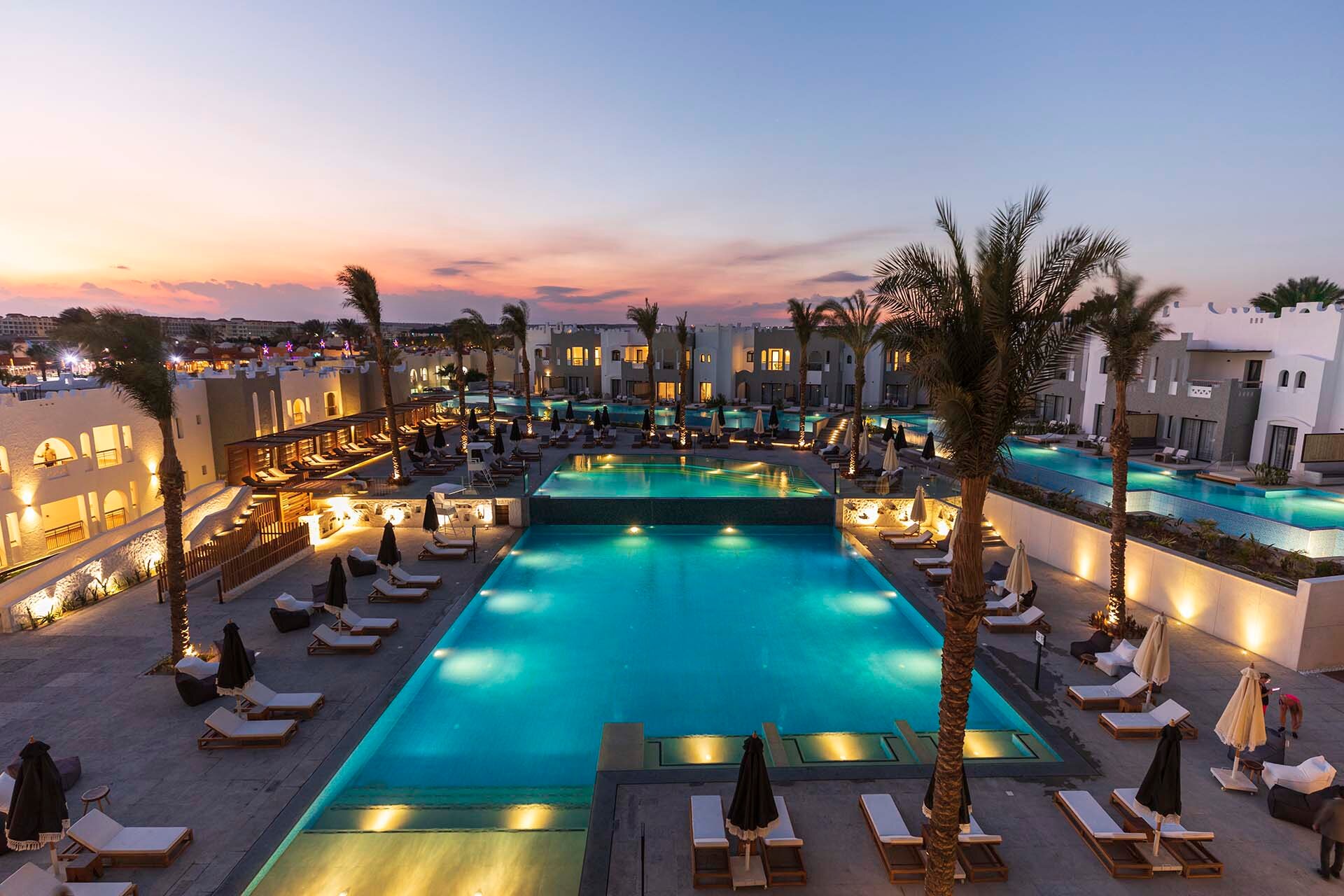 Sunrise Tucana Resort centrālais baseins ar izgaismotu ūdeni un atpūtas krēsliem vakarā, fonā moderni viesnīcas korpusi.