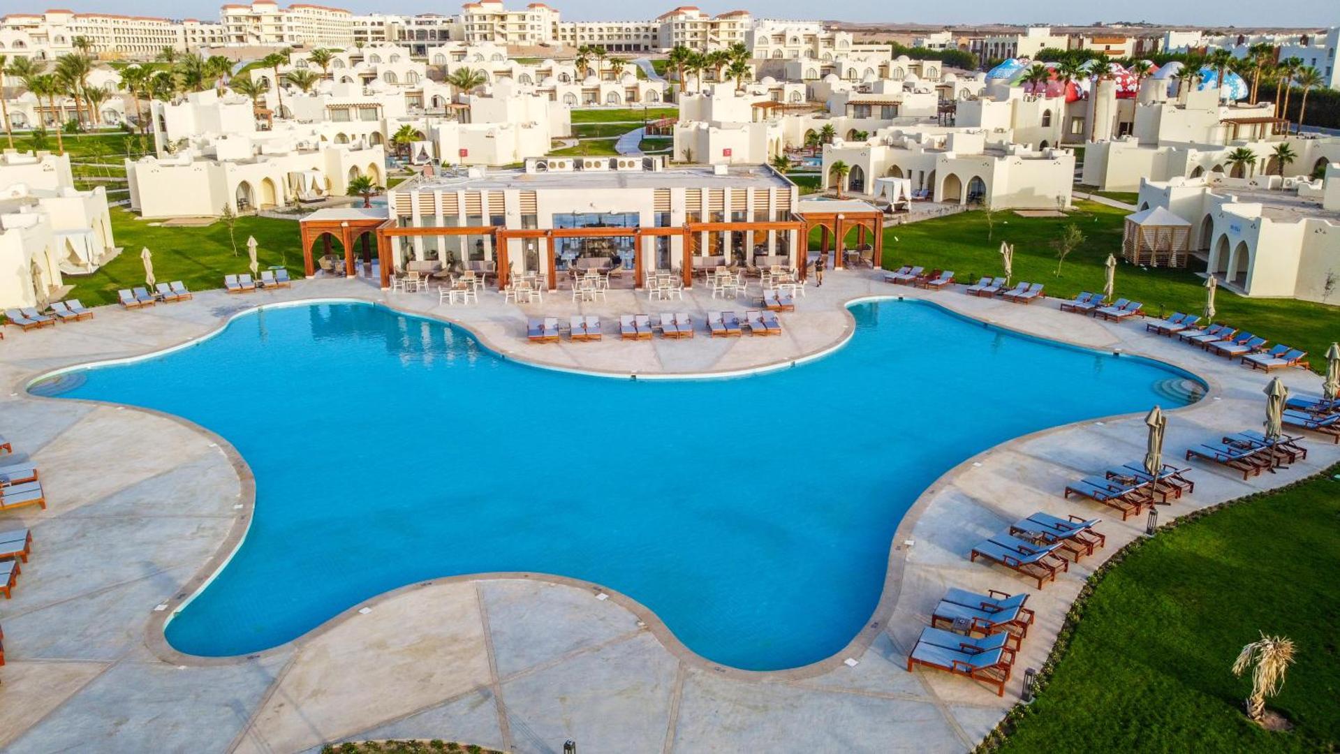 Xanadu Makadi Bay plašā teritorija ar lielu centrālo baseinu, bāru un saulessargiem — skats no augšas uz kūrorta kompleksu