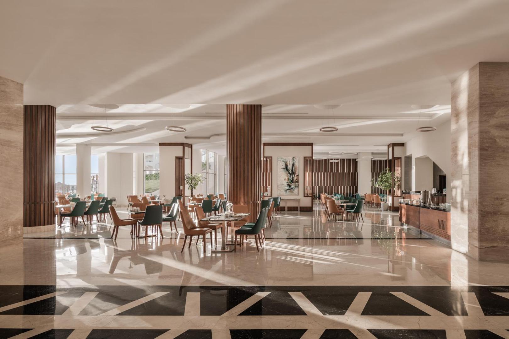 Xanadu Makadi Bay modernā viesnīcas halle ar augstiem griestiem, koka kolonnām un atpūtas zonu gaišos toņos