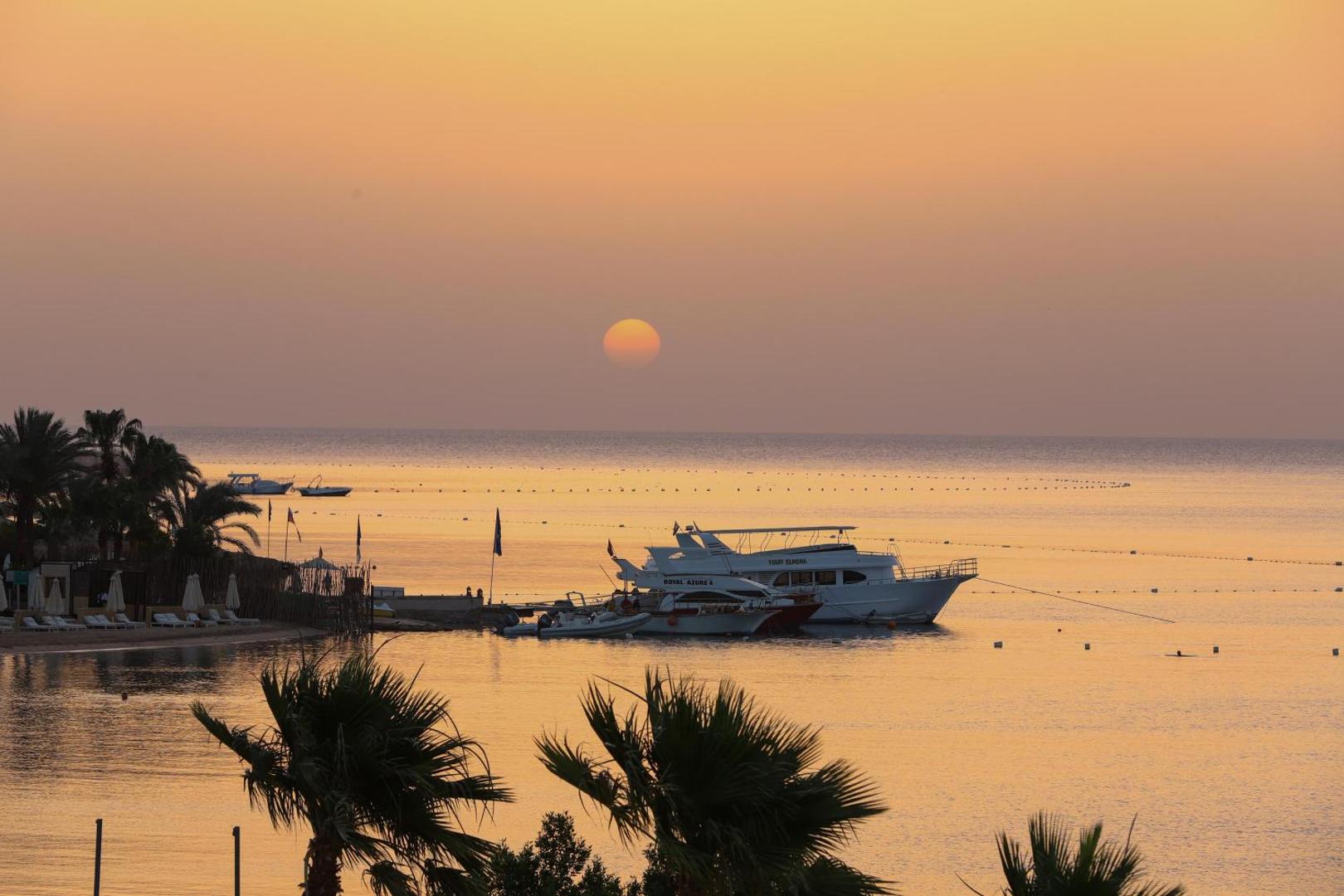 Xanadu Makadi Bay saulriets virs Sarkanās jūras Hurgadā — skats uz jahtām un palmām zeltītā vakara gaismā pie krasta