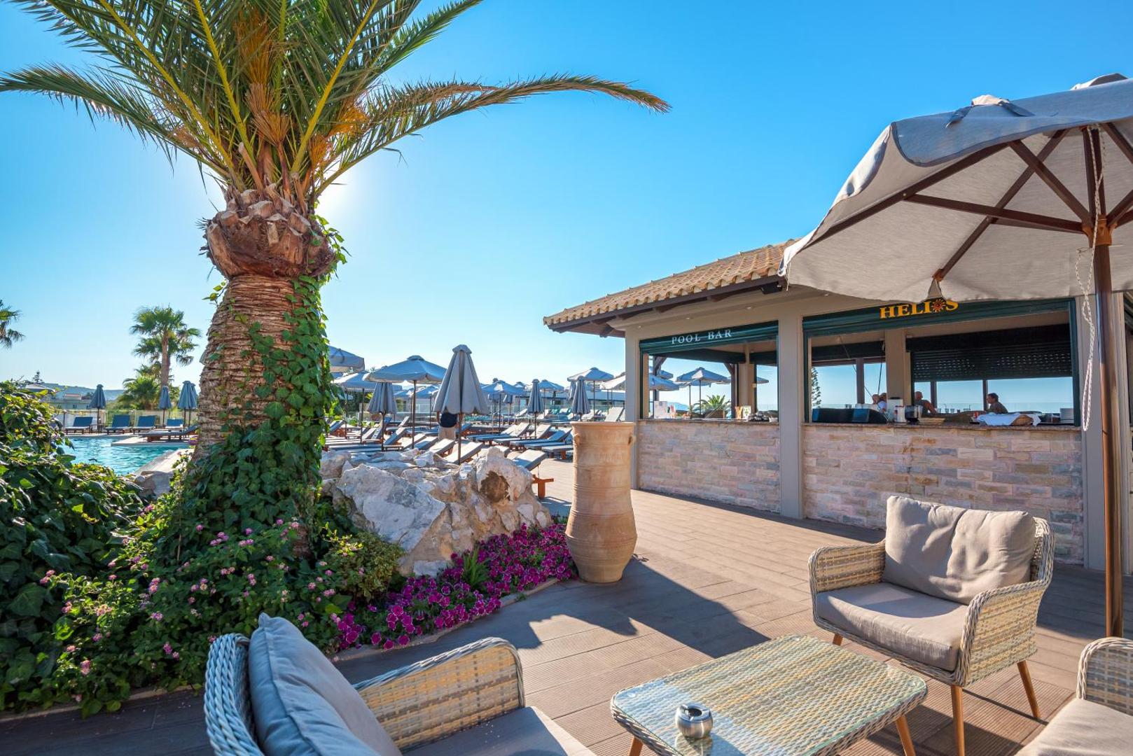 Solimar Aquamarine Resort āra bārs pie baseina Gerani piekrastē, Krētā — atpūtas zona ar pītiem krēsliem un saulessargiem palmu pavēnī