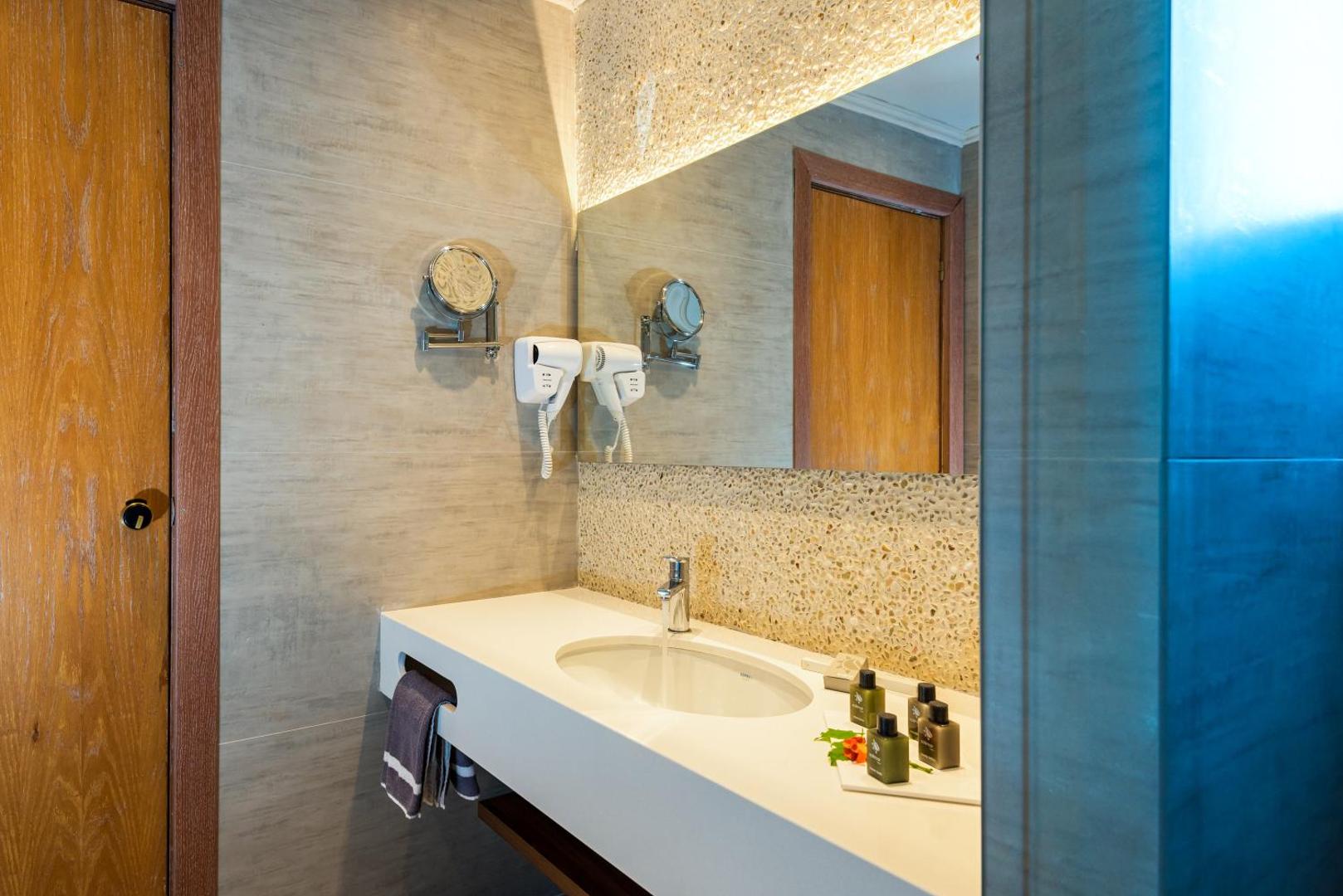 Solimar Aquamarine Resort numura vannas istaba ar modernu izlietni, lielu spoguli un higiēnas piederumiem viesnīcā Krētā
