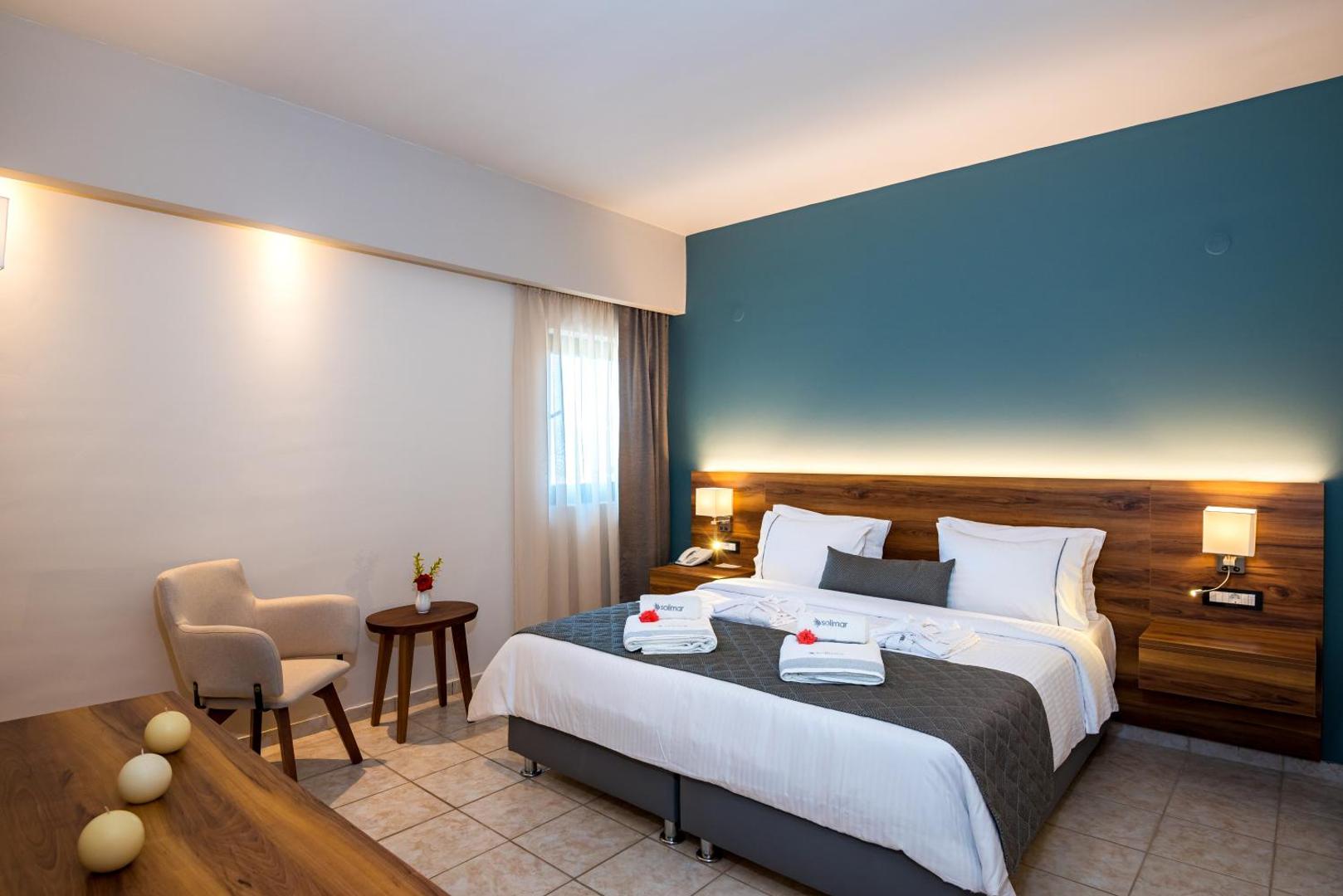 Solimar Aquamarine Resort divvietīgs numurs ar zilu akcenta sienu, lielu gultu, atpūtas krēslu un flīžu grīdu Krētas kūrortā