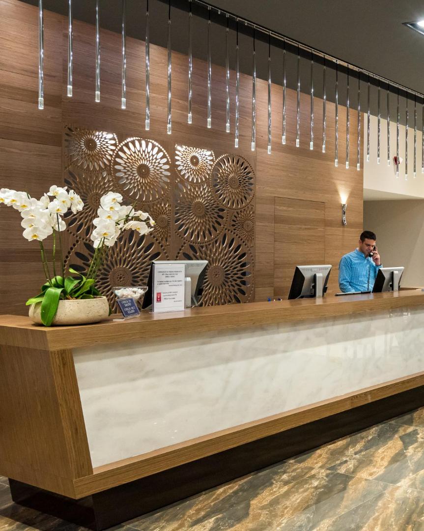 Solimar Aquamarine Resort viesnīcas recepcija ar koka apdari, modernu apgaismojumu un orhidejām, kur viesus sagaida profesionāls personāls