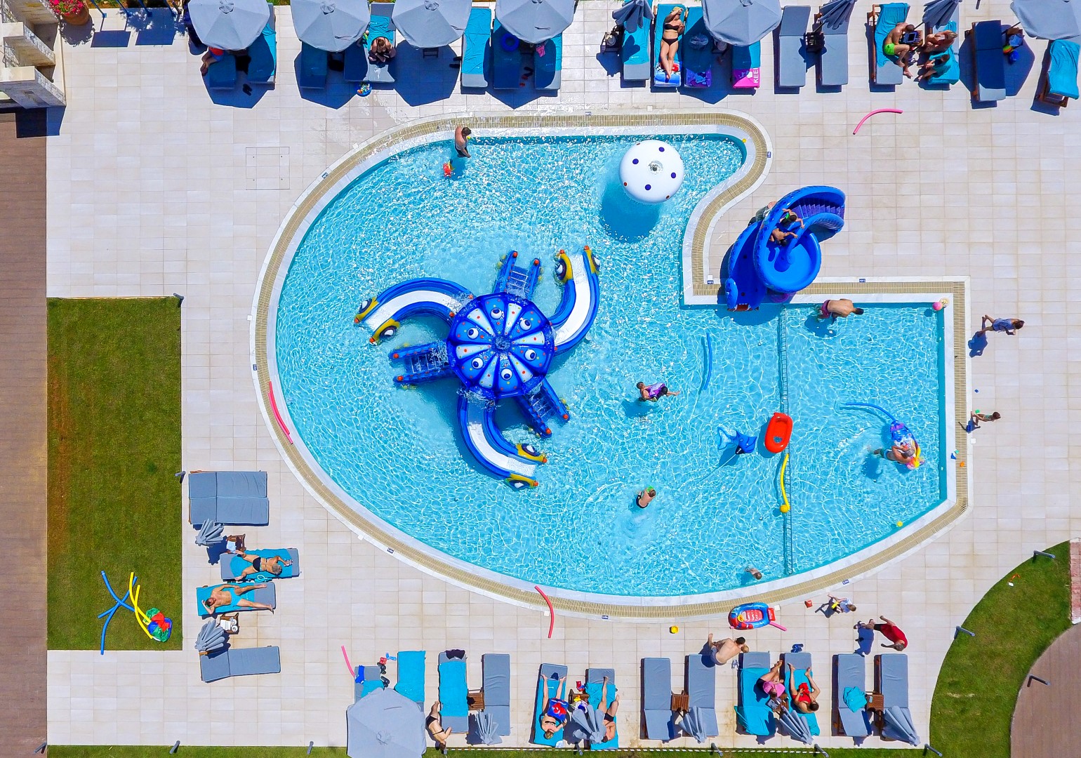 Skats no augšas uz Solimar Aquamarine Resort bērnu baseinu ar astoņkāja formas slidkalniņu un sauļošanās krēsliem Krētas kūrortā
