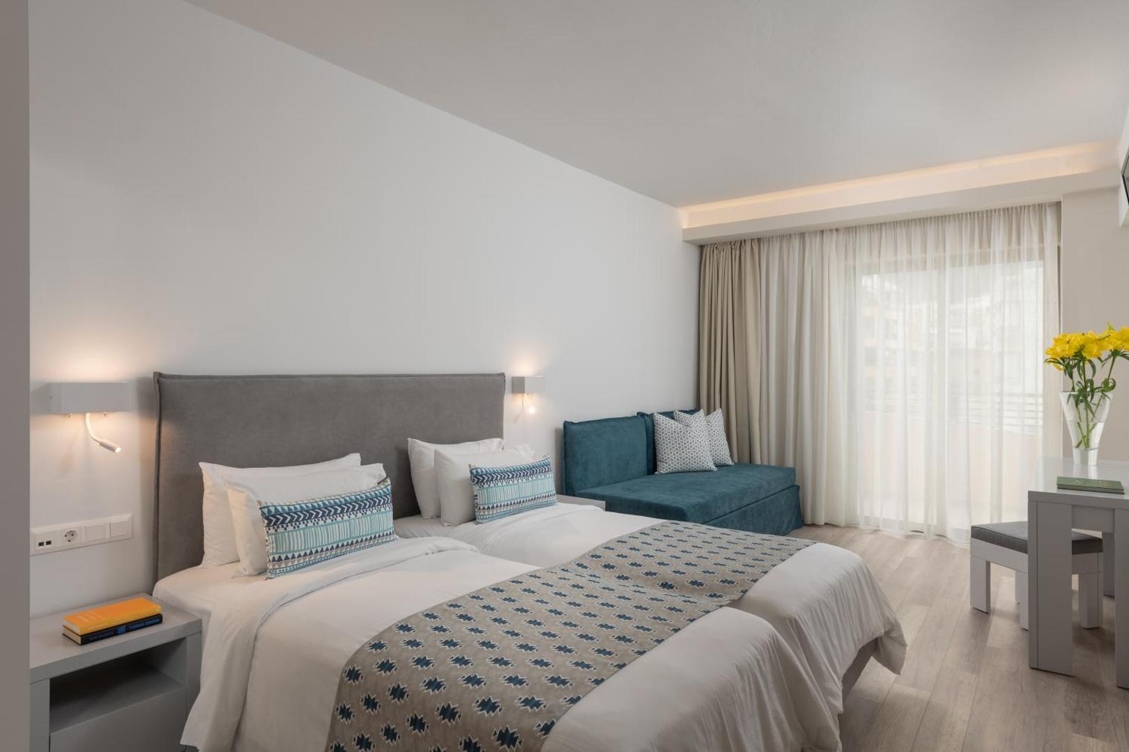 BIO Suites Hotel & Spa gaišs numurs ar divguļamo gultu, zilu dīvānu un balkona durvīm Retimno pilsētā Krētas salā