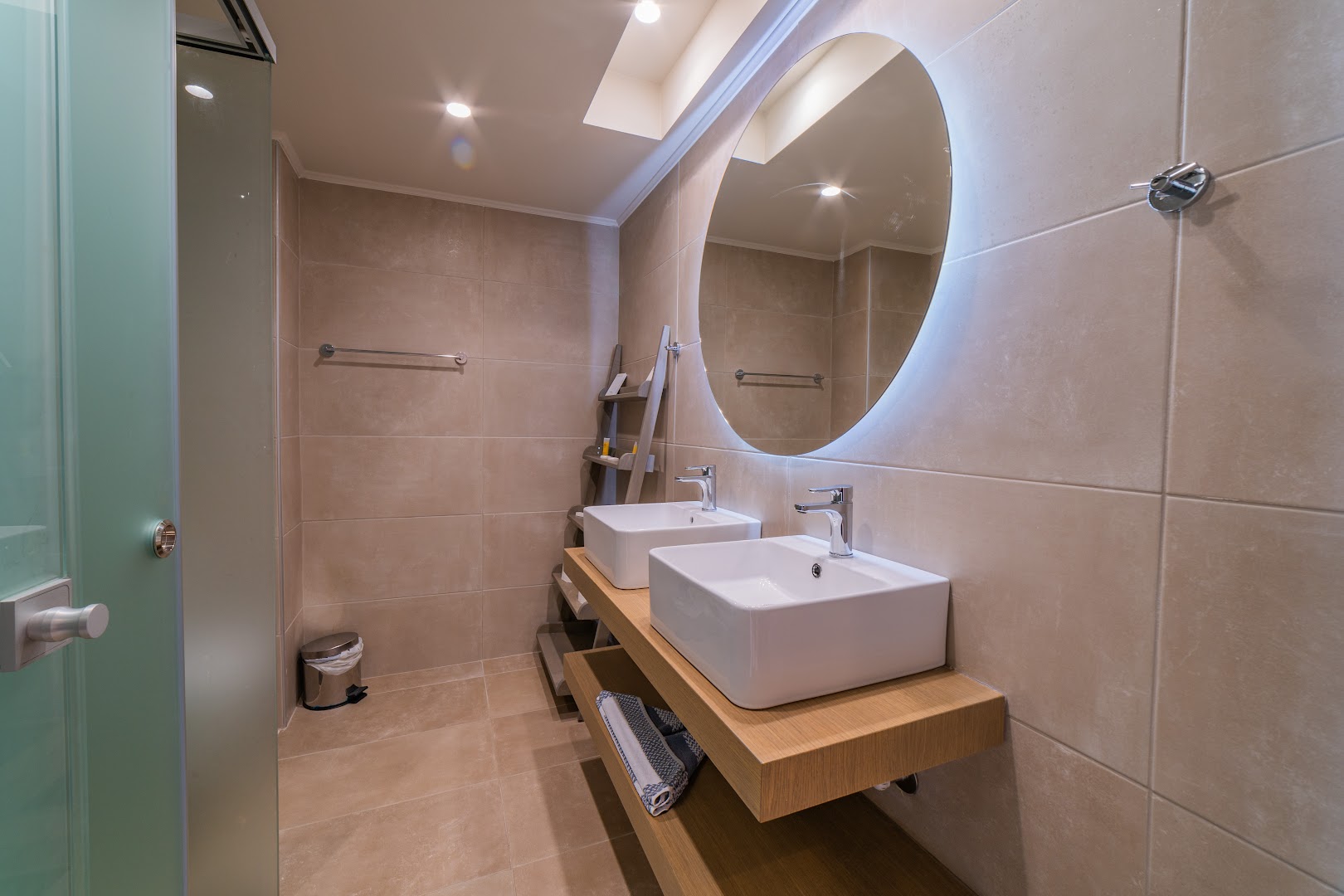 BIO Suites Hotel & Spa numura vannasistaba ar divām izlietnēm, lielu apaļu spoguli un modernu apgaismojumu smilškrāsas toņos