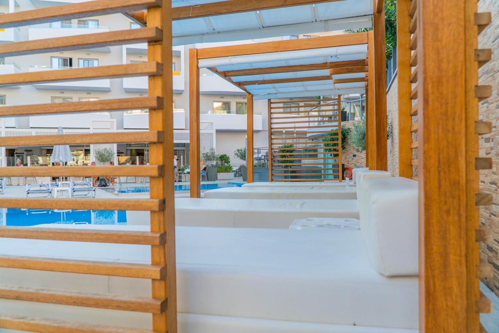 BIO Suites Hotel & Spa koka atpūtas nojumes ar mīkstiem matračiem pie baseina — komfortabla zona relaksācijai dienas laikā