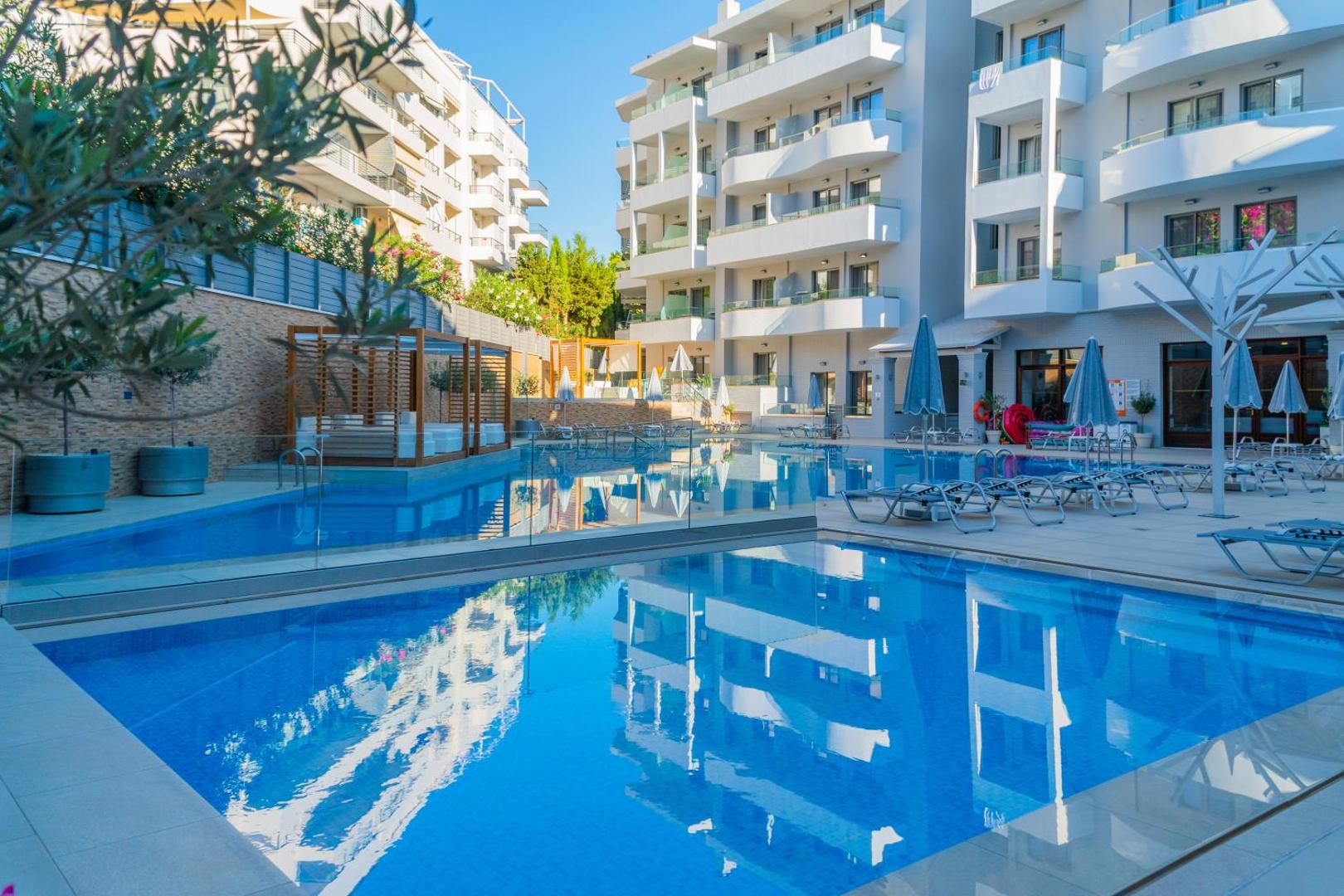 BIO Suites Hotel & Spa baseina zona ar sauļošanās krēsliem un bērnu baseinu — moderna arhitektūra un gaiši viesnīcas numuri fonā