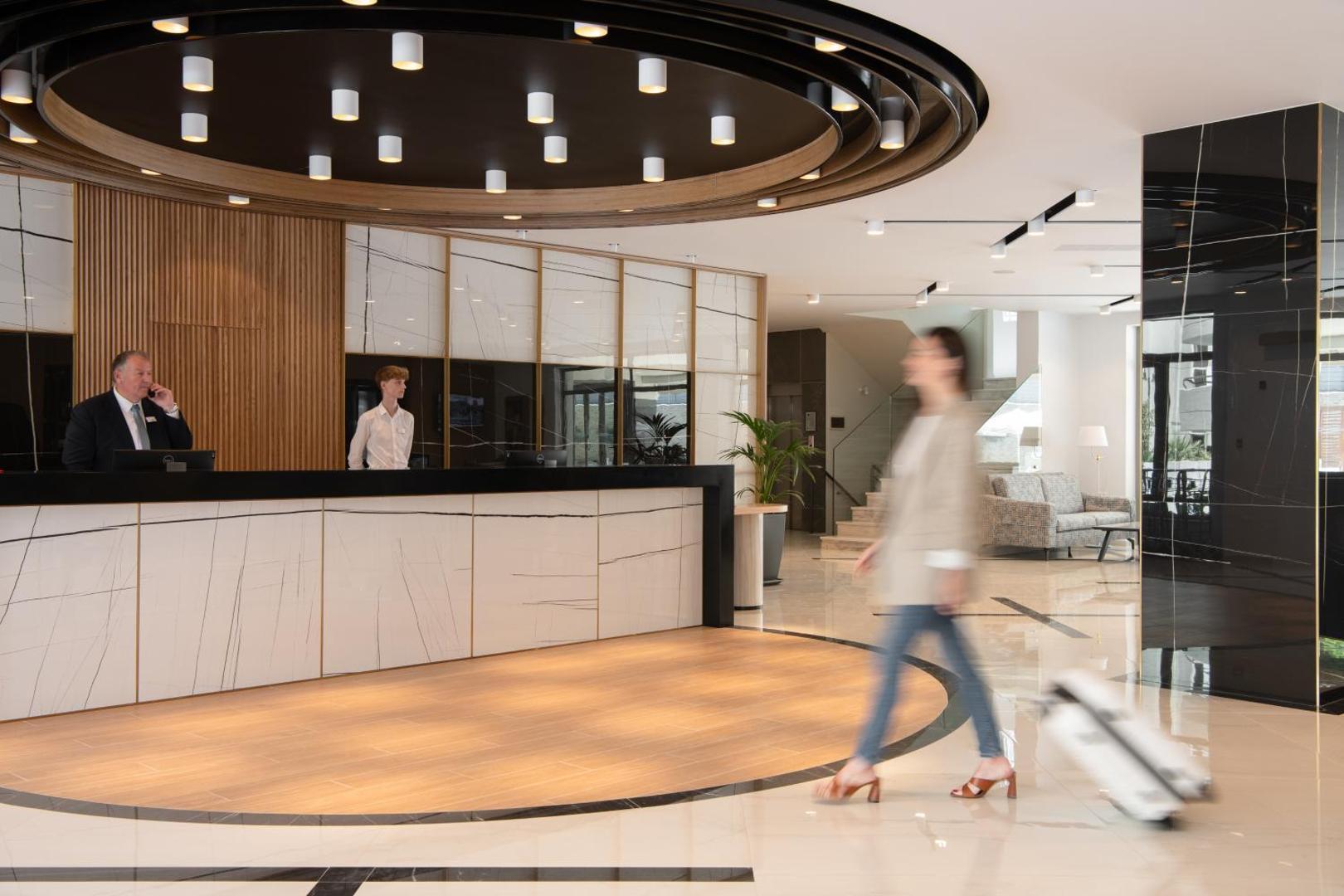 BIO Suites Hotel & Spa modernā recepcija ar marmora apdari, koka elementiem un viesmīlīgu personālu viesnīcas vestibilā.
