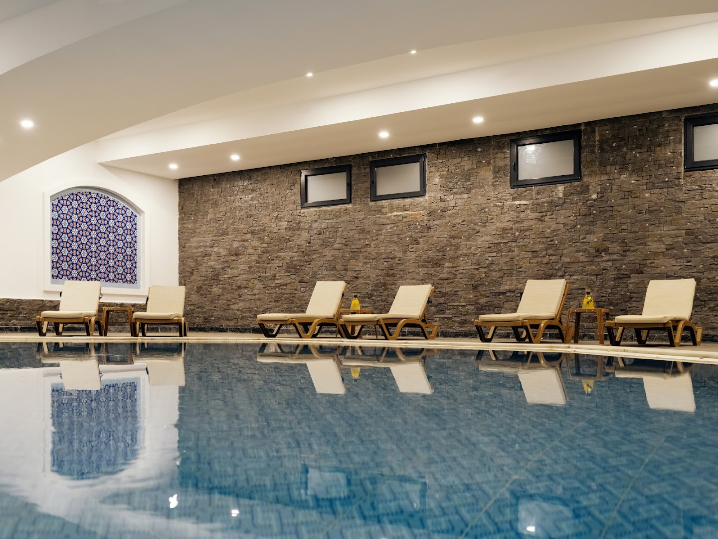 Selectum Family Resort Belek iekštelpu baseins ar akmens sienas apdari, ērtiem zviļņiem un dekoratīvu mozaīkas logu spa centrā