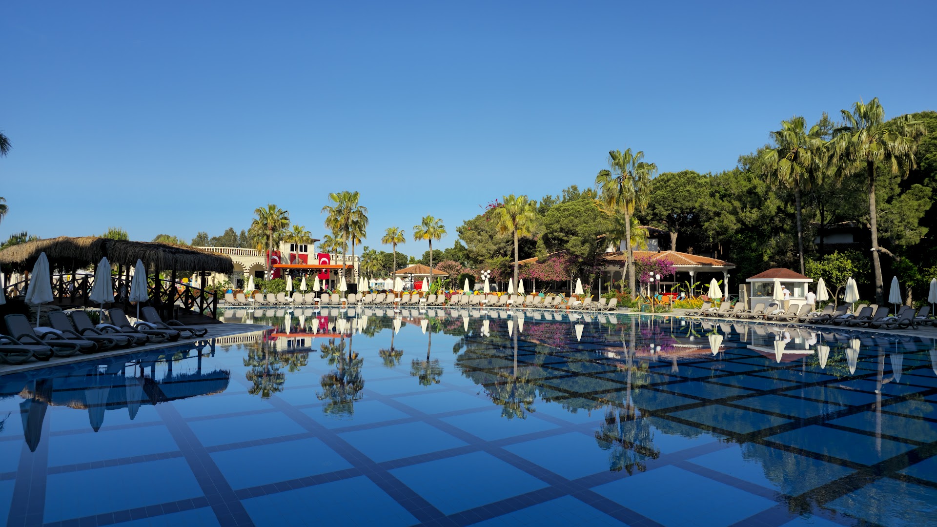 Selectum Family Resort Belek galvenais baseins ar dzidru ūdeni, palmām un saulessargiem Belekas piekrastē, Turcijā saulainā dienā.