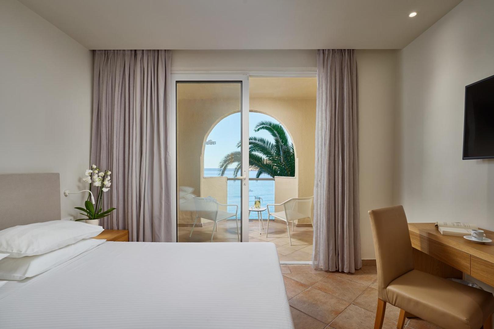 Gaišs Lindos Royal Resort viesnīcas numurs ar skatu uz jūru un palmu — mājīgs interjers un balkons Rodas piekrastē