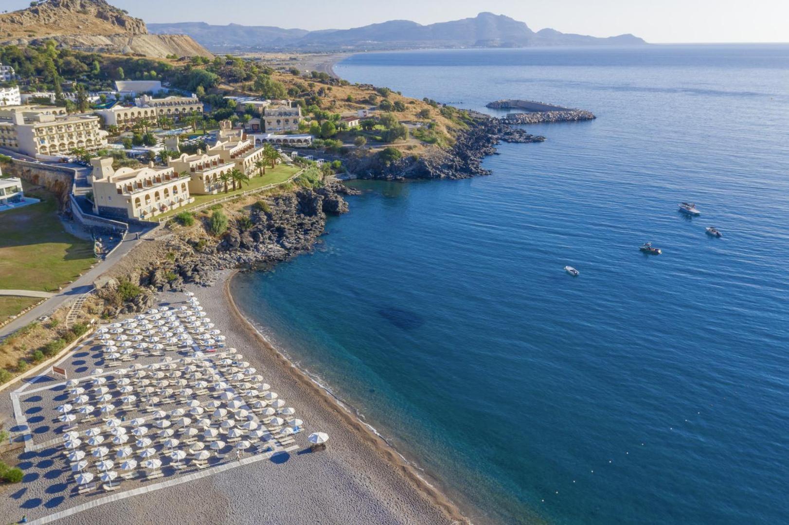 Lindos Royal Resort Rodā no putna lidojuma — viesnīcas komplekss piekrastē ar privātu pludmali, saulessargiem un dzidru Vidusjūras ūdeni