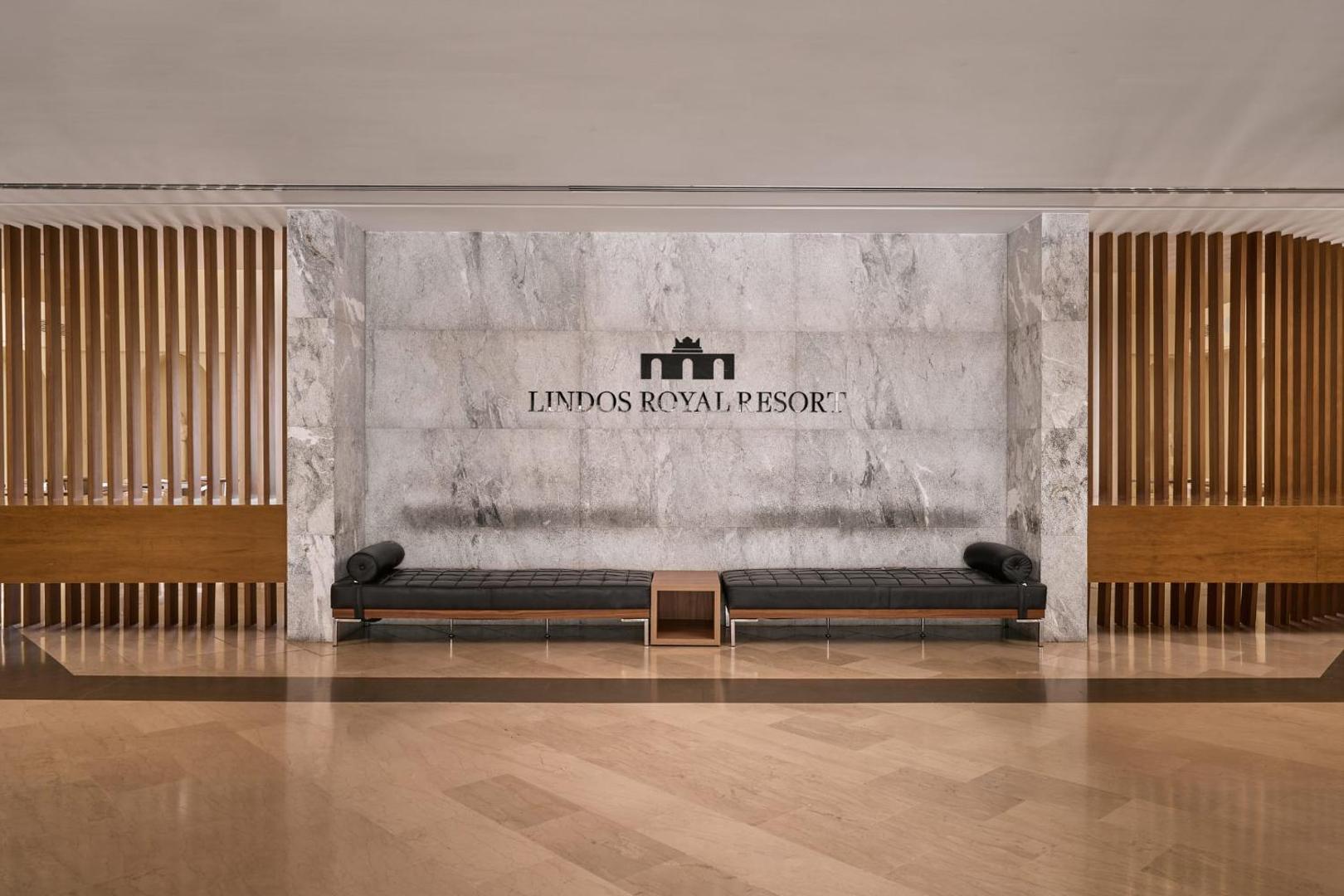 Lindos Royal Resort viesnīcas vestibils Rodas salā ar marmora sienu, logo un melniem ādas atpūtas soliem modernā stilā