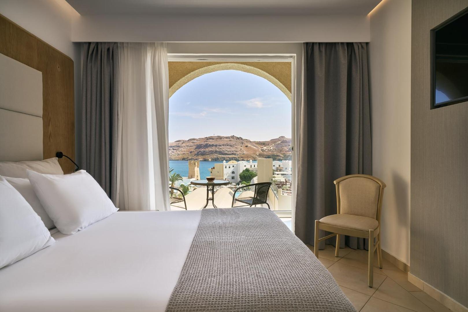 Lindos Royal Resort numura interjers ar skatu caur arkas formas logu uz Lindas līci un kalniem Rodas salā