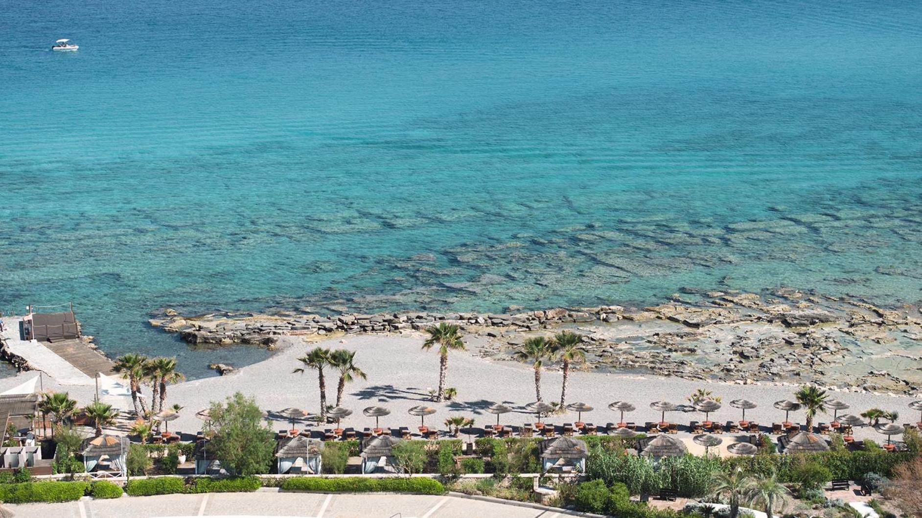 Aquagrand Exclusive Deluxe Resort skats no augšas uz privāto pludmali Rodas salā ar tirkīzzilu ūdeni, palmām un saulessargiem