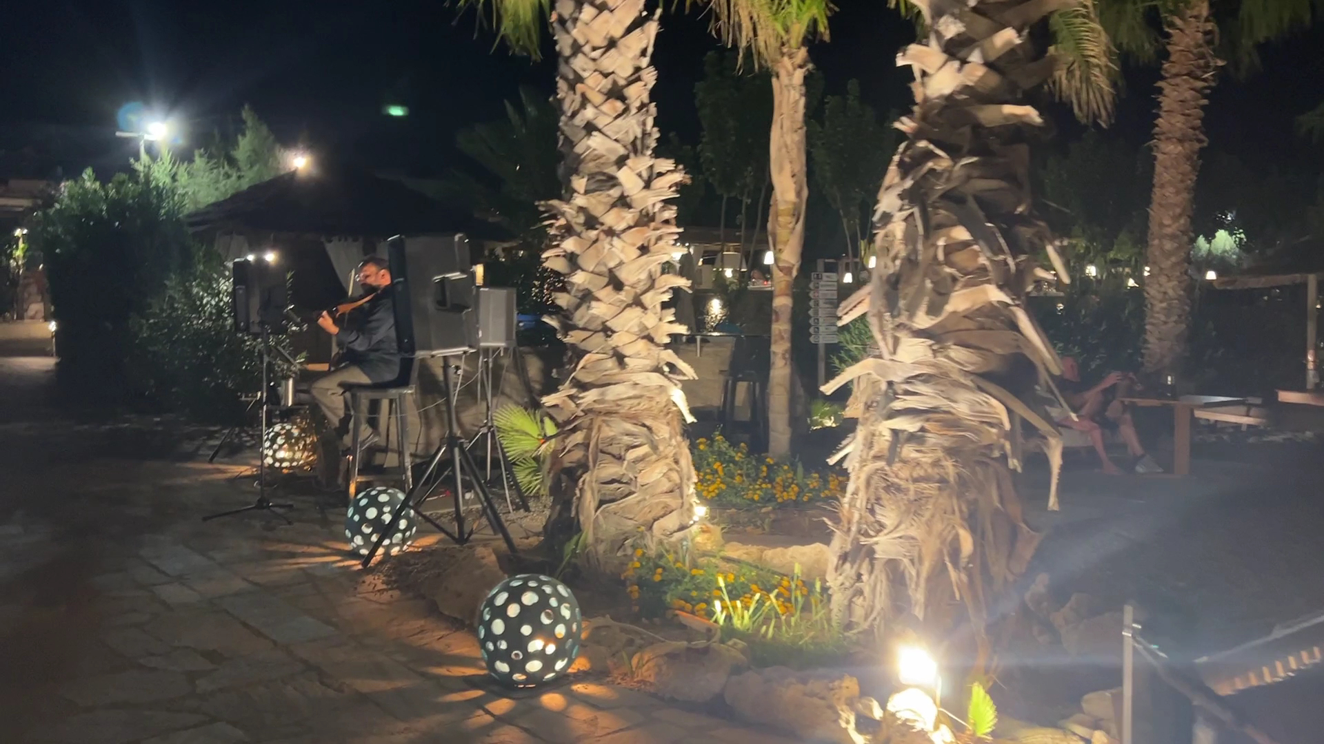 Aquagrand Exclusive Deluxe Resort dārza zona vakarā ar izgaismotām palmām un mūziķi — dekoratīvās gaismas lodes un mājīga atmosfēra