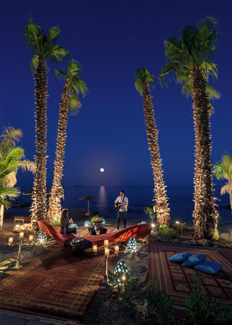 Aquagrand Exclusive Deluxe Resort pludmales zona naktī pilnmēness laikā ar paklājiem, palmām un dzīvo mūziku — romantisks iekārtojums pie jūras