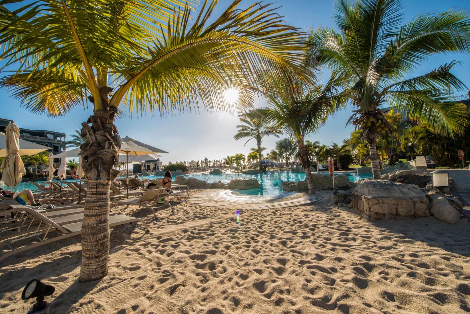 Lopesan Villa del Conde Resort & Thalasso āra baseins ar smilšu zonu un palmām Melonerasā, Grankanārijā — sauļošanās krēsli un saulessargi
