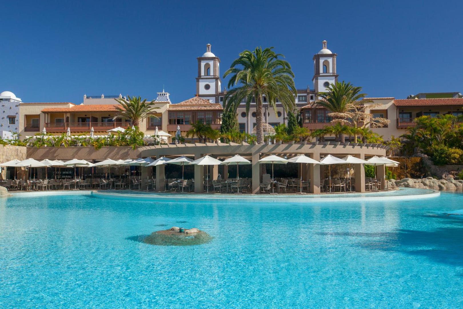 Viesnīcas Lopesan Villa del Conde restorāna terase ar saulessargiem pie liela, zila baseina Grankanārijas kūrortā