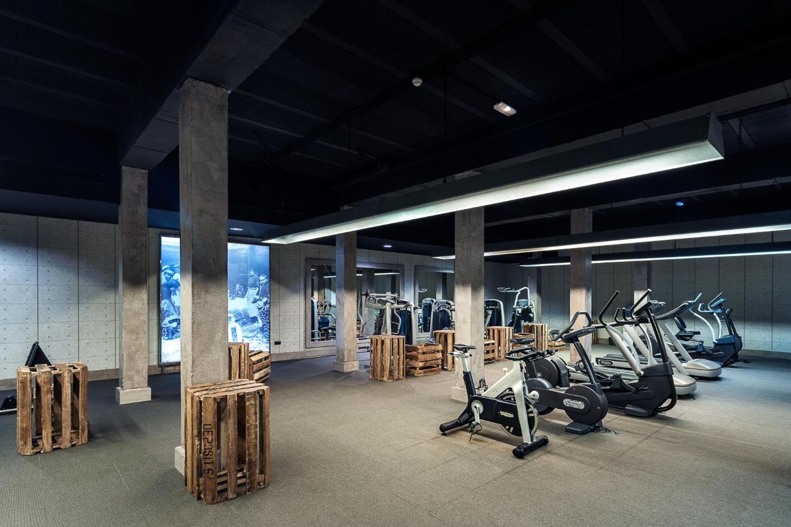 Lopesan Villa del Conde Resort & Thalasso moderns fitness centrs ar kardio trenažieriem, koka dekorācijām un industriāla stila dizainu