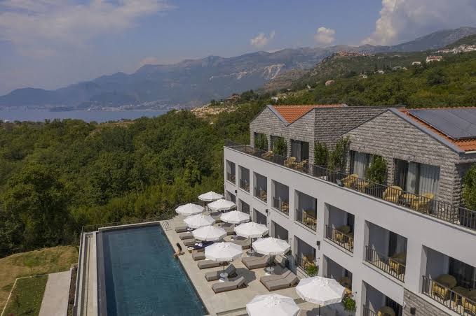 Vivid Blue Serenity Hotel skats no augšas uz āra baseinu, sauļošanās terasi ar saulessargiem un viesnīcas ēku Melnkalnes piekrastē