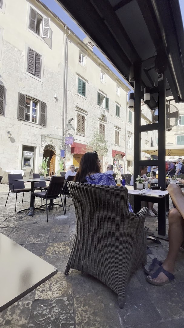 Astoria Boutique Hotel āra terase ar pītiem krēsliem uz vēsturiska bruģa Kotoras vecpilsētā, apkārt senas akmens ēkas
