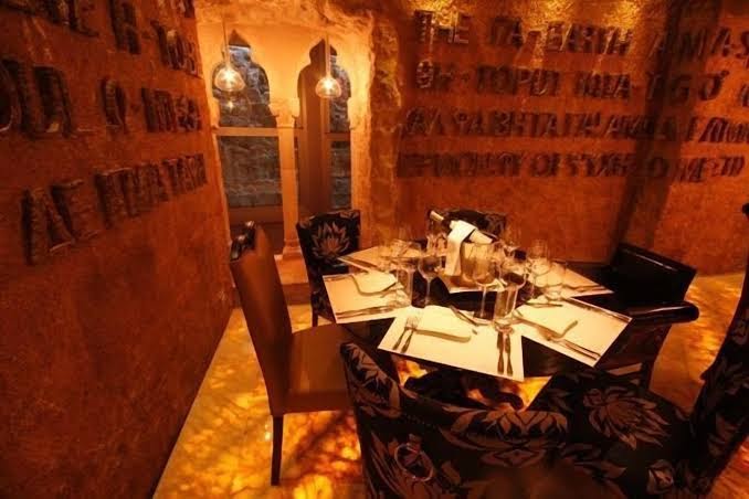 Astoria Boutique Hotel restorāna intīma zona ar akmens sienām, iegravētiem tekstiem un servētu galdiņu diviem siltā apgaismojumā