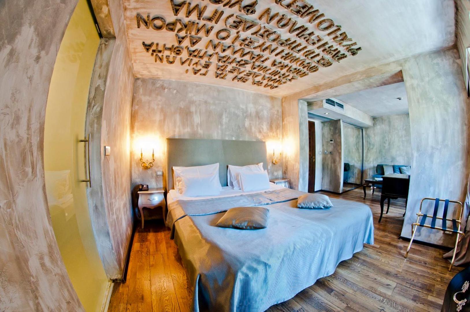 Astoria Boutique Hotel dizaina numurs ar grieķu rakstiem uz griestiem, lielu gultu un modernu apgaismojumu Kotoras vecpilsētā