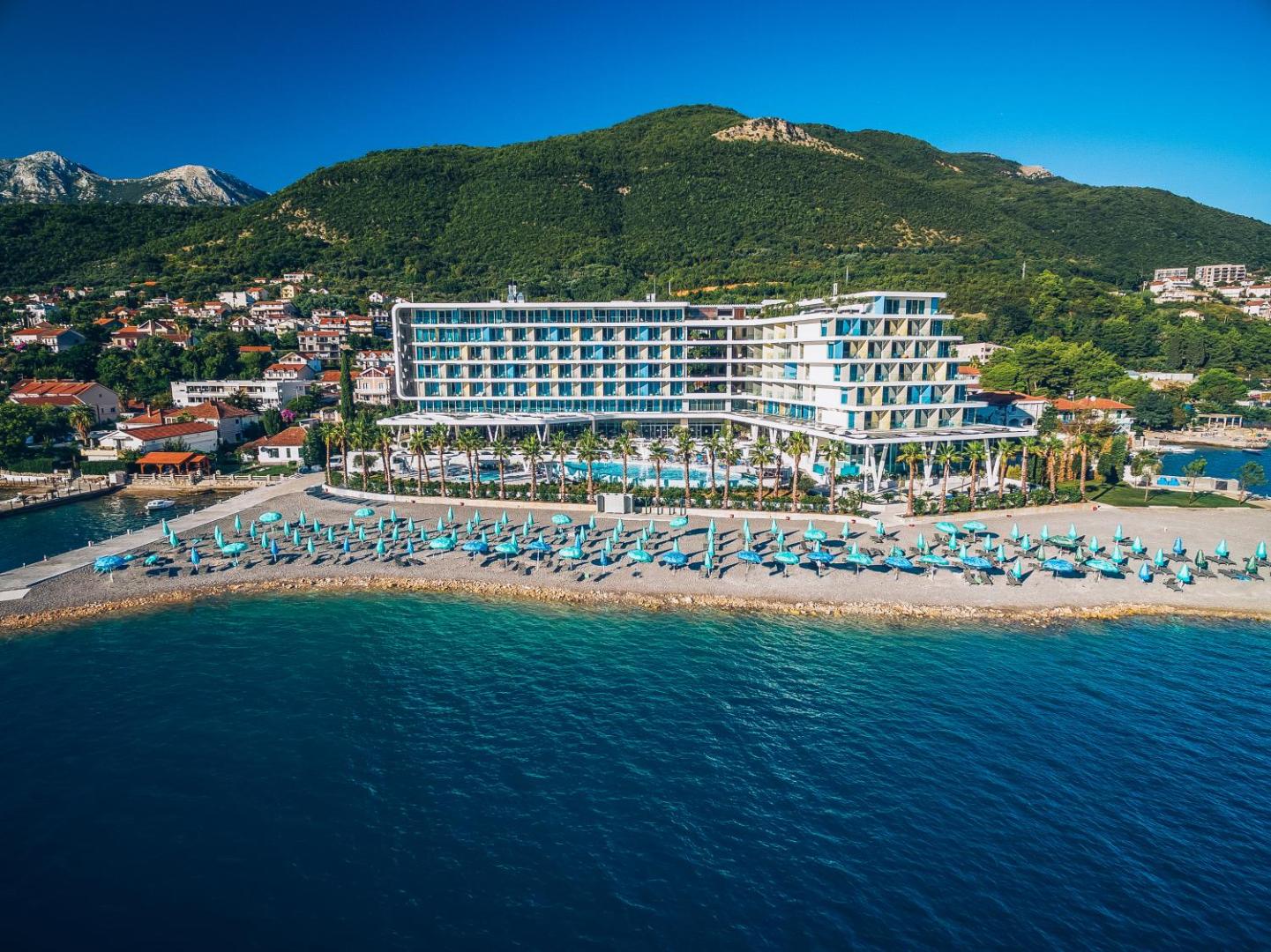 Carine Hotel Kumbor Superior skats no putna lidojuma uz viesnīcas ēku, privāto pludmali ar saulessargiem un kalniem Melnkalnē